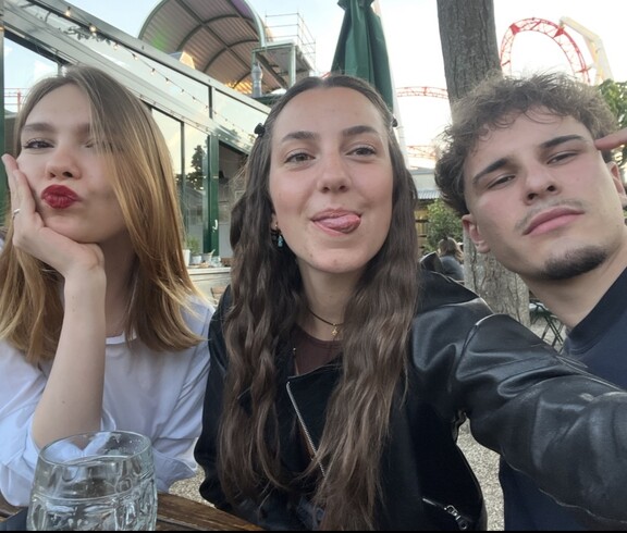 Zwei junge Frauen (eine mit Schmollmund und eine zeigt Zunge) und ein junger Mann schauen frontal in die Kamera