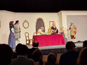 Fünf Schauspieler in Kostüm auf der Bühne, zwei sitzen an einem Tisch