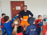 Junger Mann in gelber Latzhose ist umzingelt von mehreren Kindern in verschiedenen Kostümen.