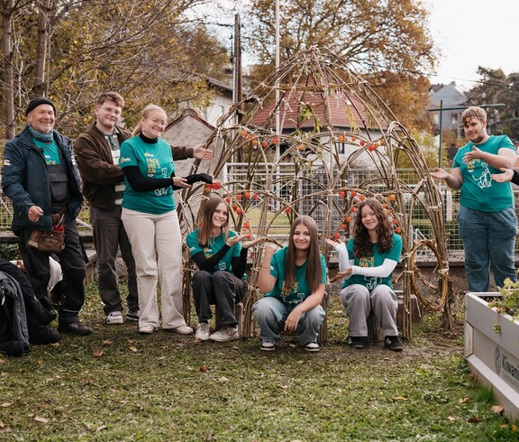 Jugendliche mit Gartenwerkzeug stehen und hocken im Garten bei Hochbeeten