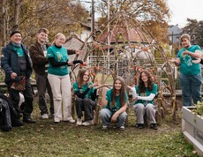 Jugendliche mit Gartenwerkzeug stehen und hocken im Garten bei Hochbeeten