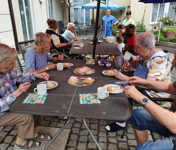 Gruppe älterer Leute sitzt beim Tisch im Garten bei Kaffee und Kuchen.