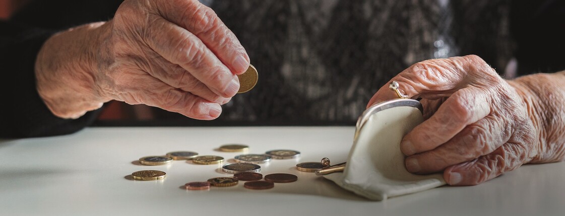 Elderly woman sitting at the table counting money in her wallet.