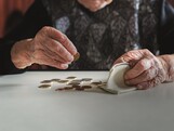 Elderly woman sitting at the table counting money in her wallet.