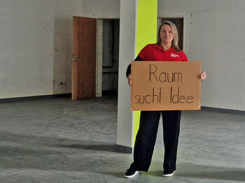 Frau steht in leerem Raum mit Schild "Raum sucht Idee"