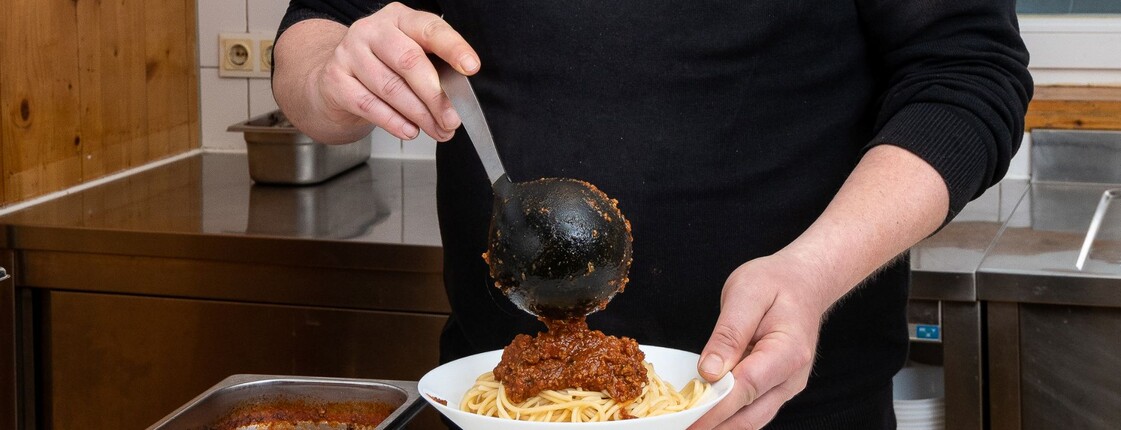 Ein Mitarbeiter des Ressidorfs schöpft Essen in einen Teller