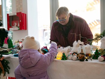 Kleines Mädchen übernimmt auf einem Weihnachtsmarkt ein Produkt von einer Frau
