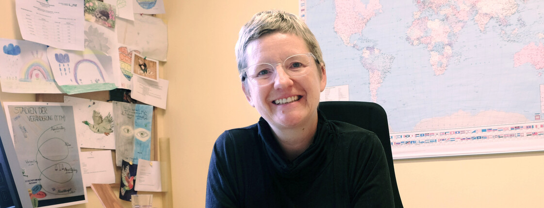 Frau sitzt vor Landkarte am Computer, dafür ein feministisches Häferl und ein Caritas&Du-Herz