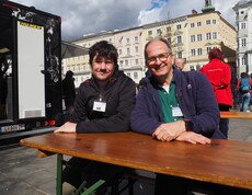 Zwei Personen sitzen auf einem Tisch auf einem öffentlichen Platz. 