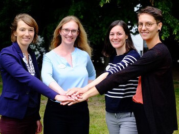 4 Personen stehen im feien zusammen und stecken die Arme nach vorne und die Hände berühren sich.