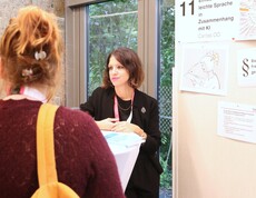 Eine Frau erklärt neben einer Pinnwand zwei Personen etwas.