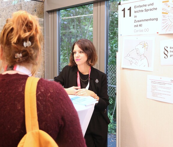 Eine Frau erklärt neben einer Pinnwand zwei Personen etwas.