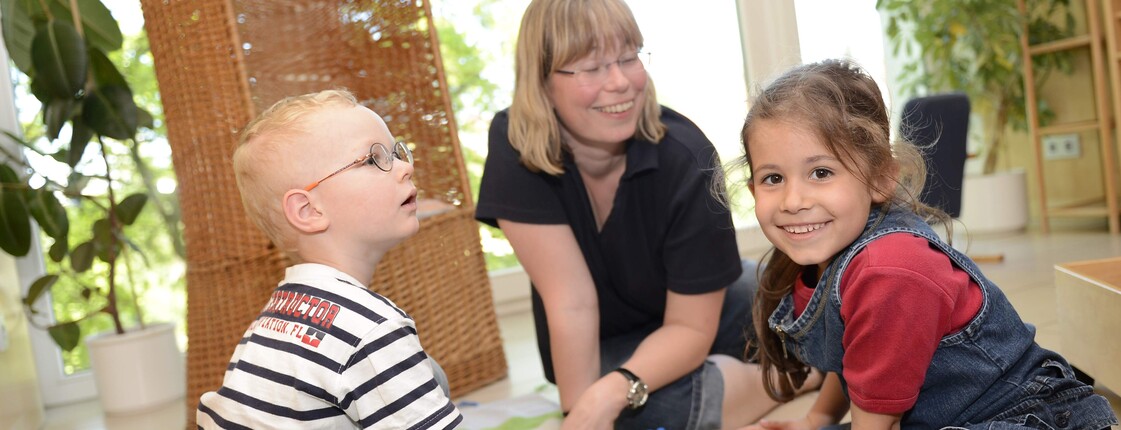 Zwei Kinder und eine erwachsene Person spielen mit Legobausteinen.