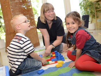 Zwei Kinder und eine erwachsene Person spielen mit Legobausteinen.