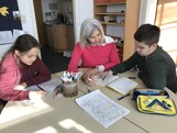 Eine Frau und zwei Kinder sitzten an einem Tisch machen Hausübungen.