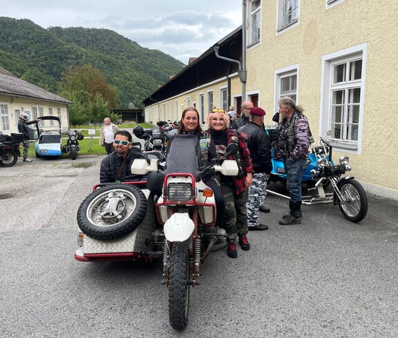 Drei Personen stehen bei einer Beiwagenmaschine. Im Hintergrund sind noch mehrer Motorräder zu sehen.