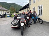 Drei Personen stehen bei einer Beiwagenmaschine. Im Hintergrund sind noch mehrer Motorräder zu sehen.