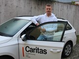 Junger Mann steht hinter offener Fahrertüre eines Autos.