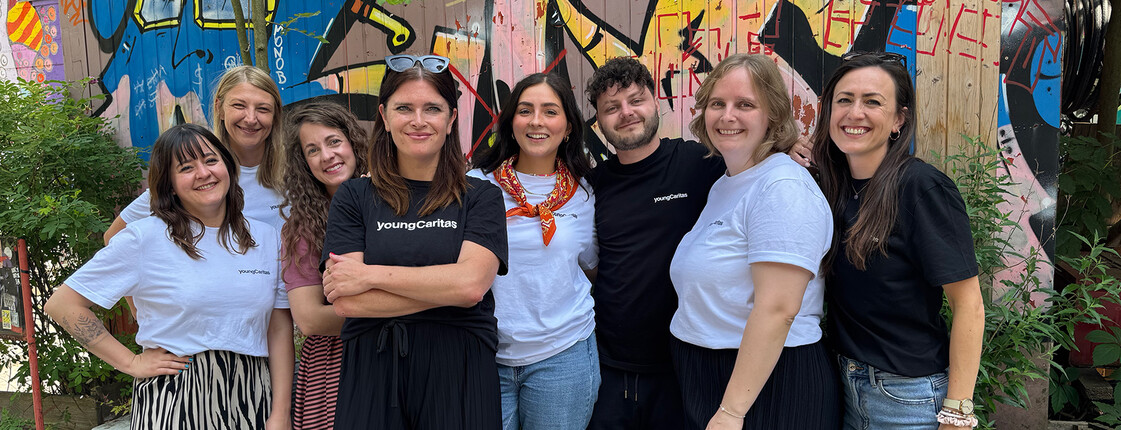 Sieben Frauen und ein Mann in weißen und schwarzen T-Shirts stehen vor einer Grafittiwand.