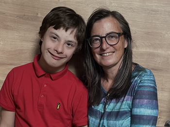 Links im Bild ein Jugendlicher im roten T-Poloshirt, rechts dabenben eine Frau mit langen braunen Haaren, einer Brille und einem blau-gestreiften Pullover