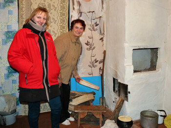 Frau in roter Jacke steht neben einem Mädchen mit rosa Wintermütze vor einem blauen Holzzaun.