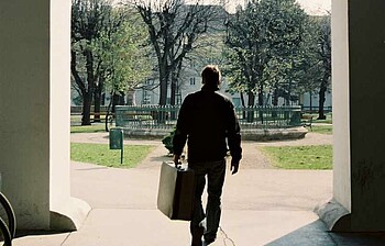 Ein Mann mit Koffer von hinten fotografiert.