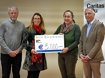 Vier Menschen, zwei Frauen und zwei Männer, stehen beisammen mit einem Spendencheck in Höhe von 5.000 Euro
