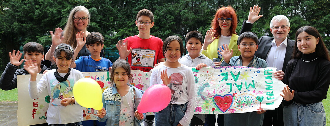 Eine Gruppe von Kindern mit Luftballons. Im Hintergrund stehen zwei Frauen und ein Mann.