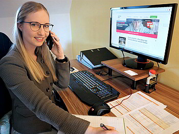 Eine Frau sitzt telefonierend am Arbeitsplatz vor dem Computer