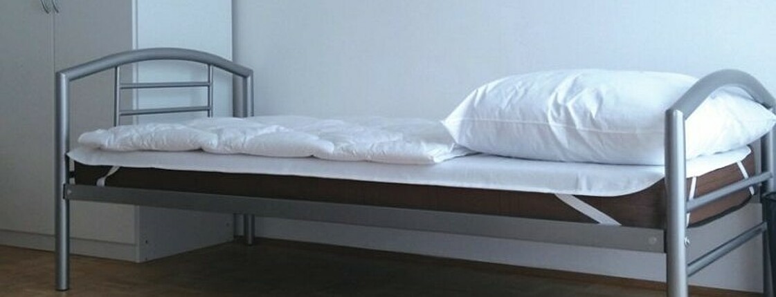 Ausschnitt eines Zimmers mit Bett und Kasten