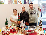 Drei Personen stehen hinter einem weihnachtlich gedeckten tisch und lächeln in die Kamera.