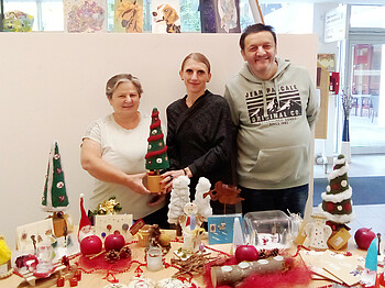 Drei Personen stehen hinter einem weihnachtlich gedeckten tisch und lächeln in die Kamera.