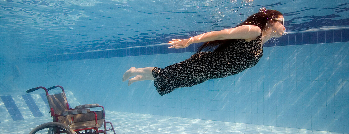 Frau im Rollstuhl schwimmt unter Wasser