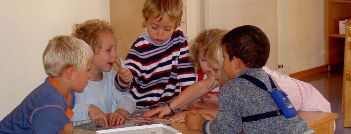 Mehrere Kinder bauen gemeinsam auf einem Tisch ein Puzzle.