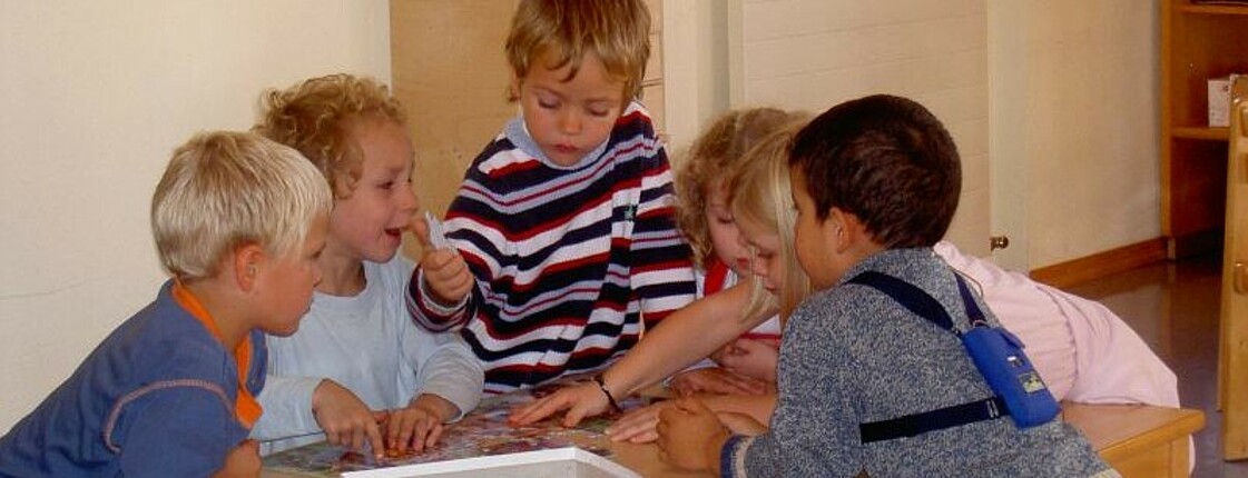 Mehrere Kinder bauen gemeinsam auf einem Tisch ein Puzzle.