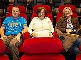 Drei Personen sitzen auf Kinosesseln und schauen in die Kamera